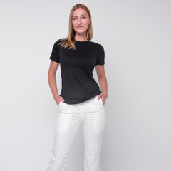 young stylish  blonde girl in white pants and black t-shirt is standing with hands in her pockets and smiling cute on the white wall background. medical concept. free space , mockup