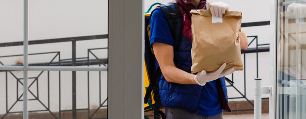 Canvas Print - Delivery Man standing with yellow thermo backpack for food delivery near the entrance home with empty space to copy paste