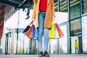 Wall Mural - Beautiful trendy young woman with many colorful shopping bags in good mood with smart phone and credit card while walking in the mall during black friday