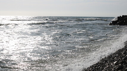 beautiful view of the sea coast, dark rocks and silver waves with a metallic shade of cloudy sky, autumn cold sea on a stone beach