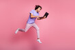 Full size profile side photo of brown haired bristled guy wear purple t-shirt pink pants hold laptop jump up run isolated on pink color background