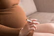 © sosiukin - Close-up of pregnant woman is holding a cigarette sitting on sofa at home