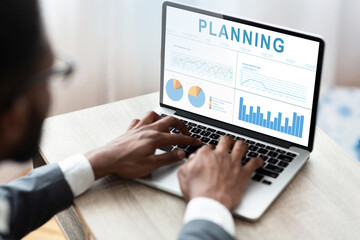 Poster - Business Planning. African Businessman Working On Laptop With Financial Graphs And Charts