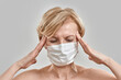 © Svitlana - Close up portrait of middle aged woman wearing white medical mask, touching her temples, having headache, feeling stress isolated against grey background