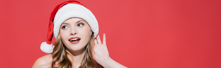  happy young woman adjusting santa hat and listening on red