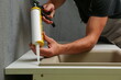 worker seals kitchen sink with sealant. hands of worker works with construction sealant gun in the kitchen.