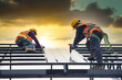 © somchai20162516 - Asian construction workers wear safety straps while working on the roof structure of the building at a construction site. Roofer, using a pneumatic nail gun, install roof tiles.
