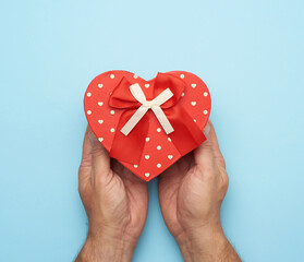 Wall Mural - male hand holding a red cardboard box with a bow on a blue background