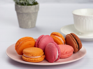 Wall Mural - baked macarons on a pink plate, behind a ceramic white cup with coffee