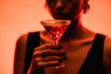 Wall Mural - margarita cocktail with ice cubes and salt in hand of woman on blurred orange background