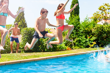 Close view of a group of kids jump with lifted hands in water pool outside during summer vacation