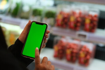 Wall Mural - close up hand tapping green screen smart phone in grocery store. Blur background