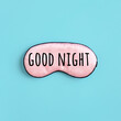 Good night text on pink silk sleep mask for eyes on blue background. Top view Flat lay. Concept eye protection from light for good sleep and melatonin production