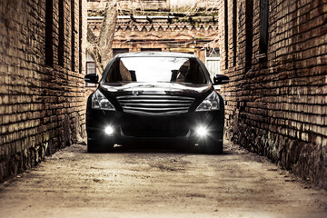 A large black car passes between two old brick buildings