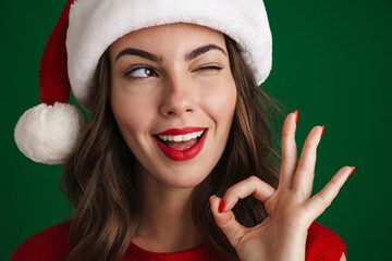 Sticker - Beautiful happy girl in Santa Claus hat winking and showing ok sign