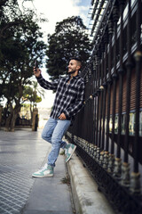 Wall Mural - Young handsome European man in a plaid patterned shirt taking a selfie in the street