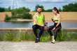© Georgii - Athletic smiling young couple in stylish sportswear after workout sitting with phone and bottle of water outdoor