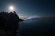 © Christian Tisdale/Stocksy - A person shining a bright flashlight into the night sky over the ocean