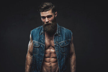 Muscular and self-confident guy with naked torso and beard with modern haircut posing in dark background.