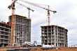 © MaxSafaniuk - Cement  mixer truck working pouring mix into crane concrete bucket. View of larger construction site where tower cranes are building residential buildings, multi-storey offices and modern skyscrapers