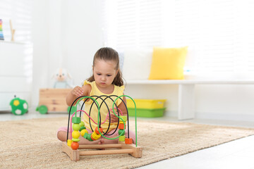 Wall Mural - Cute little girl playing with bead maze on floor at home, space for text. Educational toy