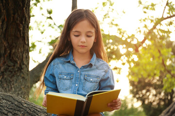 Cute little girl reading book on tree in park