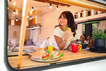 Sticker - Young woman having breakfast in trailer, view from outside. Camping vacation