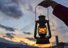 Female's Hand Holding A Lantern With The Beautiful Sunset In The Background
