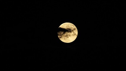 full moon rising behind clouds against dark sky