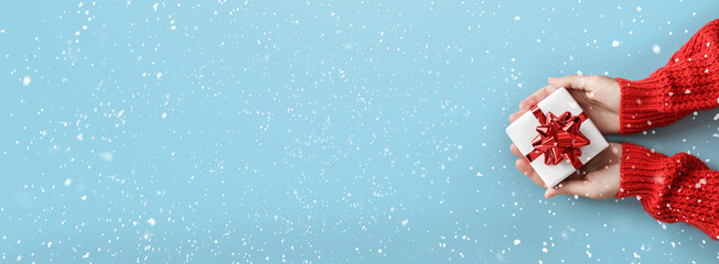 Wall Mural - female hands holding christmas gift box with red bow on light blue background with snowflakes. xmas 