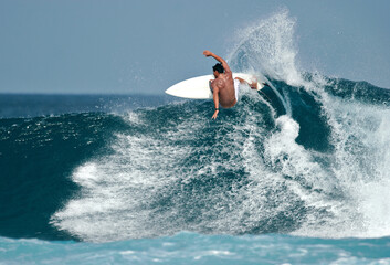 a surfer carves a radical off-the-lip on a beautiful blue wave in the ocean.