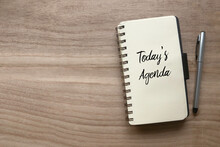 Top View Of Pen And Notebook Written With Today's Agenda On Wooden Background With Copy Space.