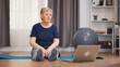 © DC Studio - Old woman sitting on yoga mat stretching body watching exercise lesson on laptop. Retired old person learning new tehnology lessons online using laptop, healthy lifestyle combined with sport