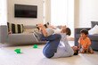 © Mangostar - Little boy lying on dad legs and spreading hands. Happy lovely boys playing with father on carpet in living room. Caucasian man lying on floor and holding boy. Childhood and game activity concept