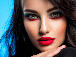 Wall Mural - Portrait of beautiful young woman with bright blue makeup. Beautiful brunette with bright red lipstick on her lips. Pretty girl with long black hair. Closeup face of brunette woman. Sexy girl.