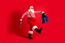Full Length Profile Photo Of Grandfather Grey Beard Walk Hold Mask Fins Wear Santa Claus X-mas Costume Suspenders Sunglass Striped Shirt Hat Boots Isolated Red Color Background