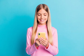 Poster - Photo portrait of smiling blonde little girl using smartphone app typing texting isolated on vivid turquoise color background