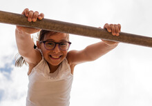 Closeup Portrait Of A Cute Happy Girl Hanging From A Monkey Bar In A Playground