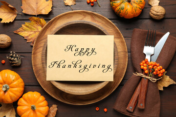 Seasonal table setting with Happy Thanksgiving Day card and pumpkins on wooden table, flat lay