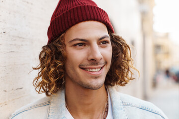 Sticker - Smiling young curly man walking outdoors by street.