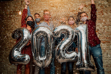 Wall Mural - Happy group of friends with face mask celebrating new 2021 year - Confetti falling in the air - Young people with balloons in hands making new year party at home - Focus on balloons.