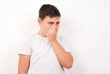 Caucasian Young Boy Standing Against White Background , Holding His Nose Because Of A Bad Smell.