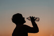 © Shiv Mer - Silhouette of an Indian kid drinking water from the water bottle in front of sun during the sunset, Drought of water concept