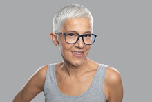 Smiling Senior Woman With Short White Hair And Glasses Posing In Front Of Gray Background