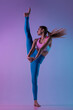 Stretching. Young sportive woman training isolated on gradient studio background in neon light. athletic and graceful. Modern sport, action, motion, youth concept. Beautiful caucasian woman practicing