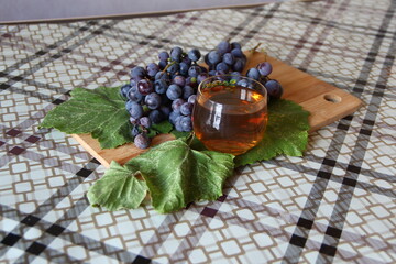 Blue grape bunches with leaves and glass of wine on a table