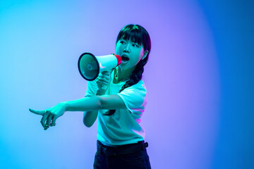 Wall Mural - Shouting with loudspeaker. Young asian woman's portrait on gradient blue-purple studio background in neon. Concept of youth, human emotions, facial expression, sales, ad. Beautiful brunette model.