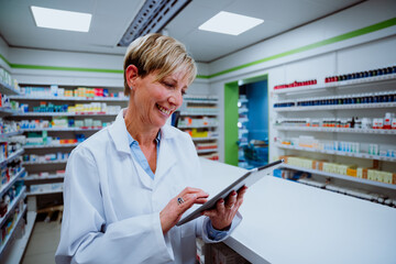 Wall Mural - Caucasian pharmacist scrolling on digital tablet standing by medication counter in pharmacy 