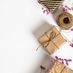 Wall Mural - gift box wrapped in kraft paper, notebook and pink flowers on white background. flat lay styling.