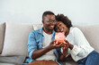 © Dragana Gordic - Multiracial couple holding piggy bank and hugging, mortgage for young families. Smiling Young Couple Sitting On Sofa Holding Pink Piggybank.
